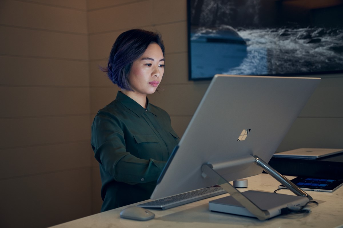 Side profile of a woman wearing a dark shirt in a dim office working on a Microsoft Surface Studio.