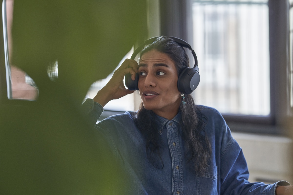 Employee in modern work space lifting headphones to hear someone speaking out of frame.