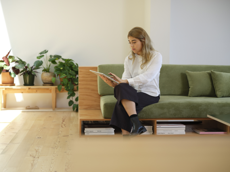 A woman sitting on a couch, working on a tablet.