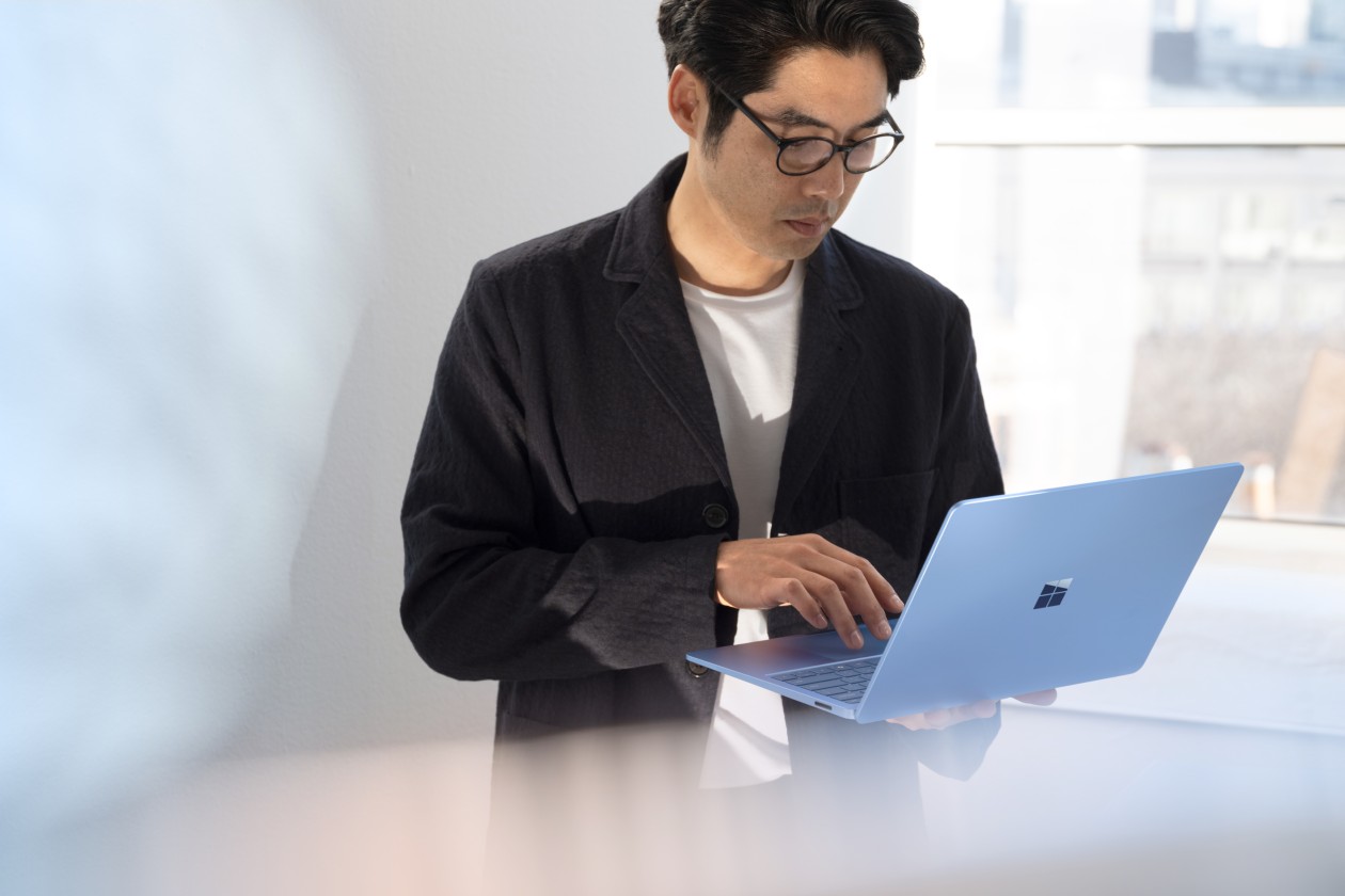 A man in a black jacket, standing and working on a laptop that he's holding