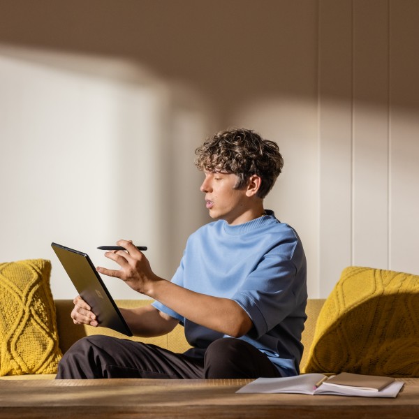 A young man sitting on a couch holding a tablet and a stylus