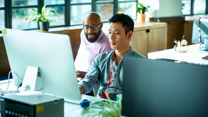A group of men looking at a computer screen in an office.